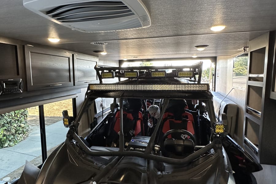 A powerful Can-Am Maverick UTV, equipped with LED light bars, is securely parked inside an RV rental toy hauler.