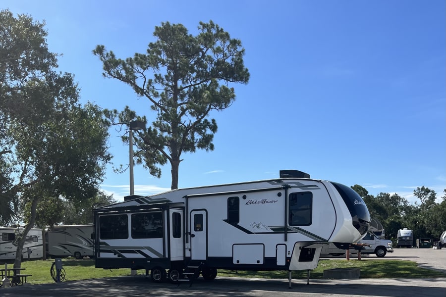 White Eddie Bauer fifth-wheel RV parked at a sunny campground. This impressive camper highlights the appeal of an RV rental.