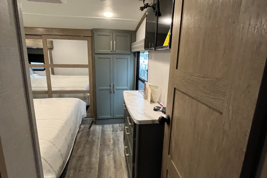 Inside an RV rental: a compact yet comfortable bedroom area with a bed, dresser, mounted TV, and built-in storage.