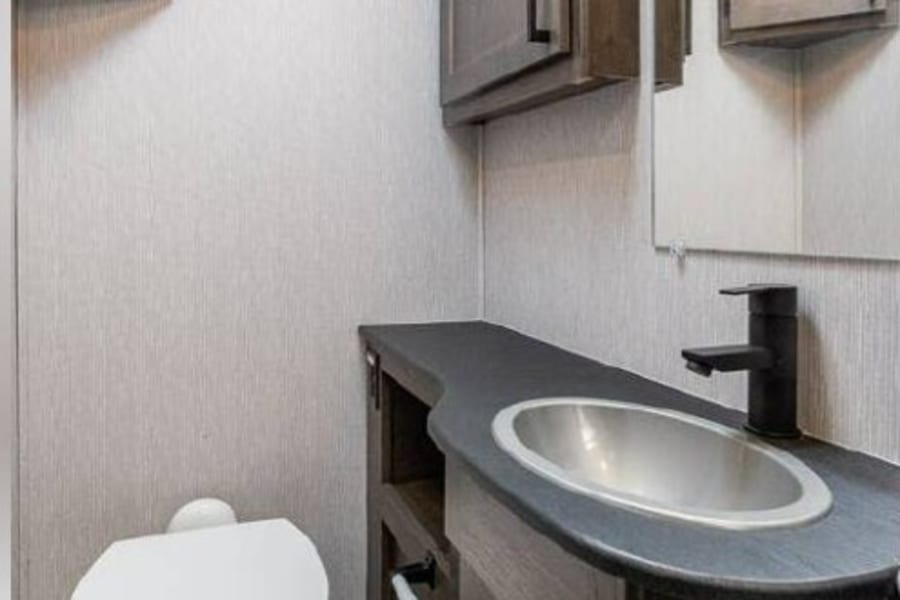 Compact RV rental bathroom featuring a modern sink vanity, toilet, and storage cabinets.