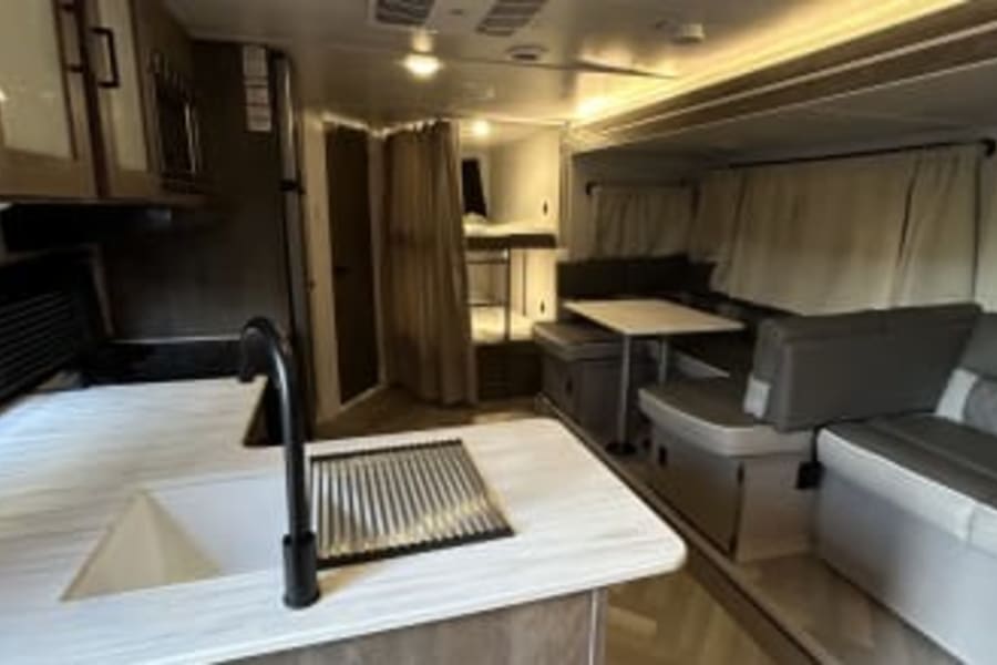 Explore this spacious RV rental interior, featuring a well-equipped kitchen, comfortable dining area, and cozy bunk beds.