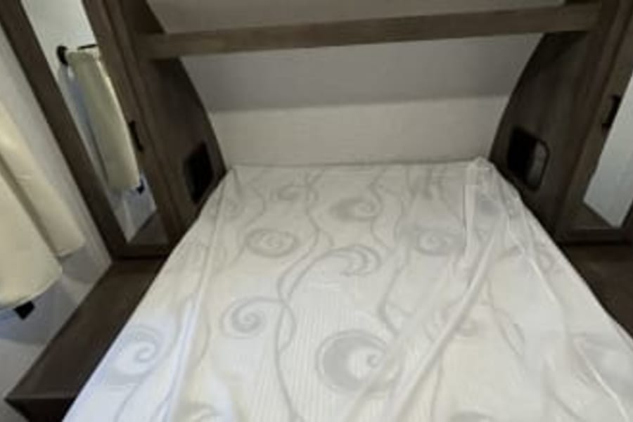 This RV rental shows a compact bedroom. A white, patterned bed is centered with wood shelving/cabinets surrounding it, perfect for travel.