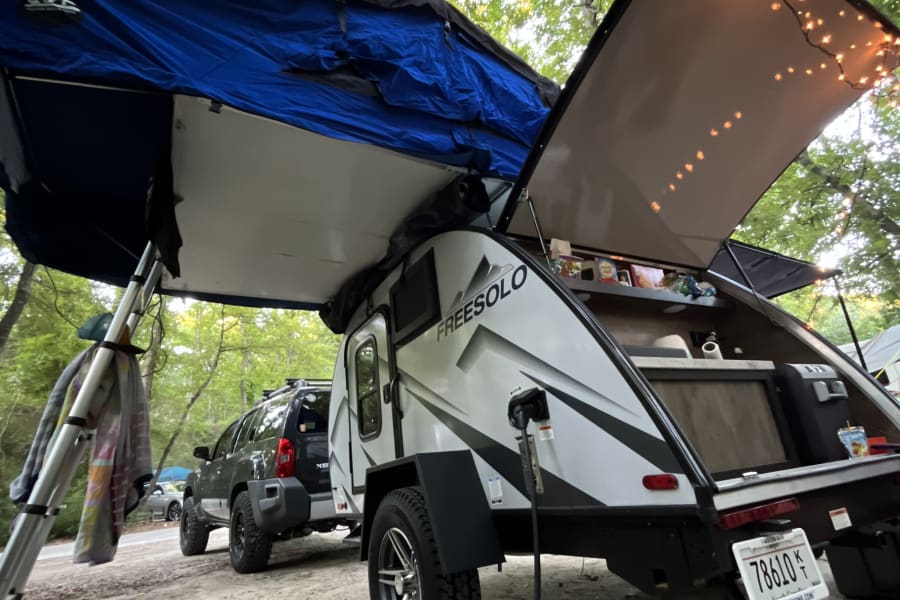 FREESOLO teardrop RV rental & SUV with rooftop tent set up at a leafy campsite for outdoor adventure.
