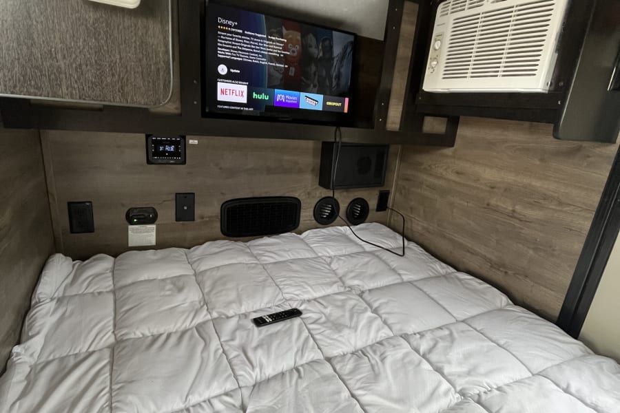 This RV rental offers a compact bedroom with a comfy bed, TV, AC, and climate controls for a cozy stay.