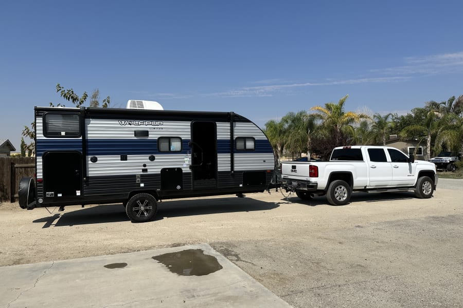 A white GMC pickup truck towing a Wolf Pup travel trailer on a sunny day. Perfect for your next RV rental trip!