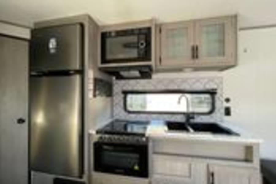 A compact yet fully equipped RV rental kitchen, featuring a modern fridge, microwave, range, and sink.