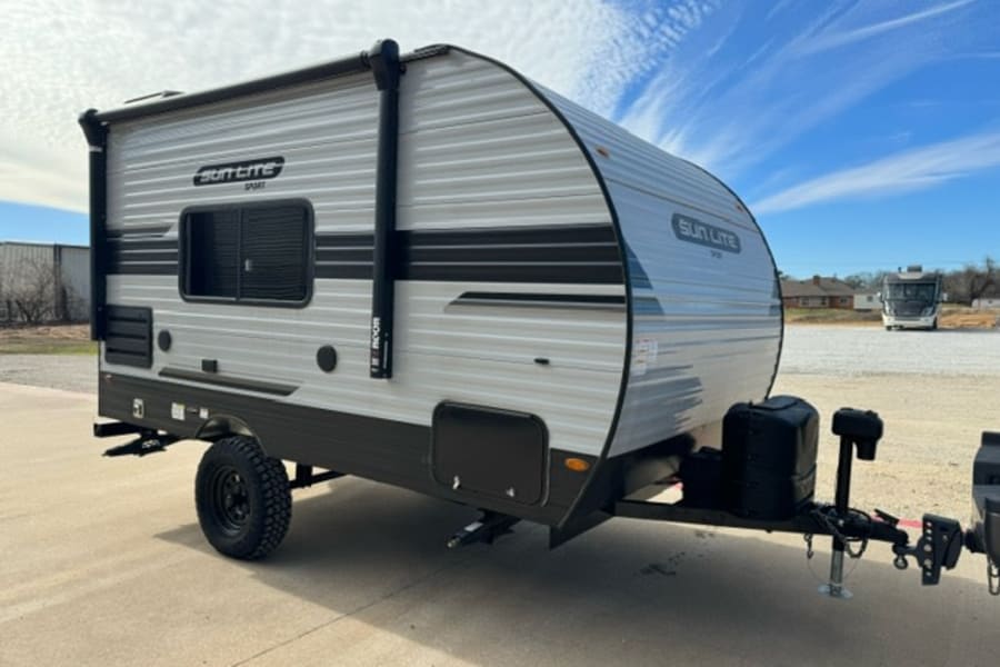 This compact grey Sun Lite Sport travel trailer with rugged tires is available for RV rental, perfect for outdoor camping adventures.