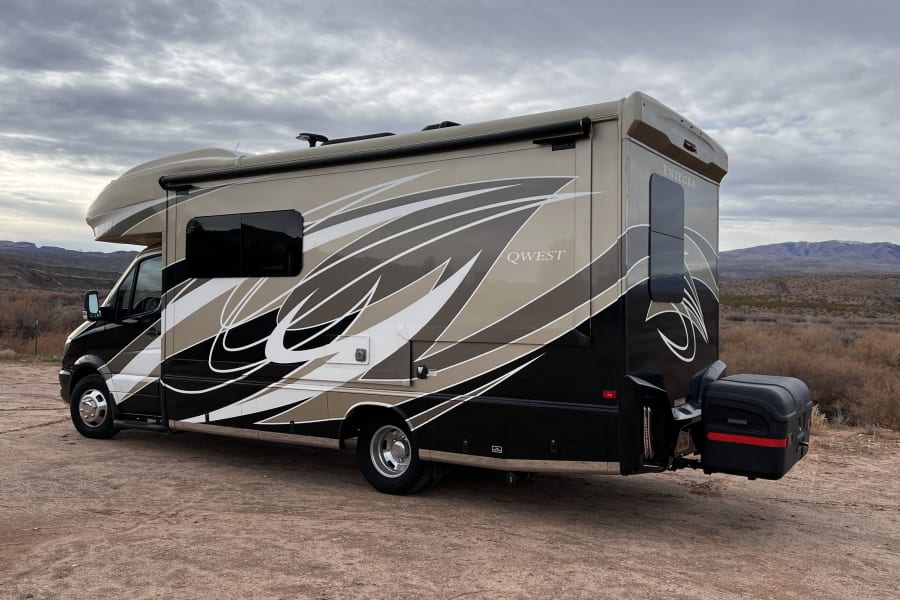 Experience adventure with this QWEST Entegra RV rental. A beige, black, and white motorhome parked on a dirt road in a scenic desert.
