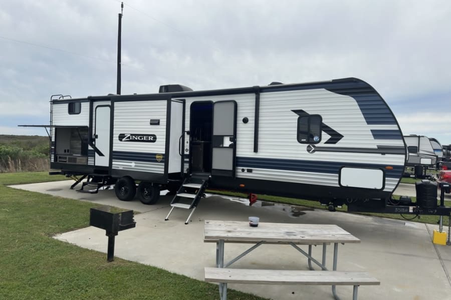 Spacious RV rental set up at a campground site with an outdoor kitchen, picnic table, and grill.