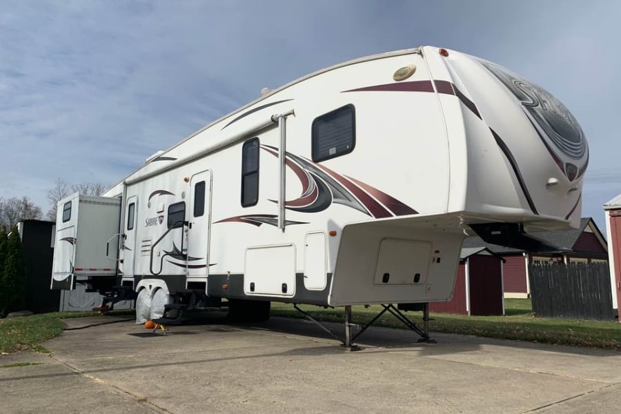 White Sabre fifth-wheel RV parked on a driveway with slide-outs extended, ideal for an RV rental getaway.