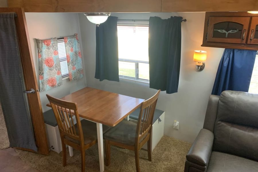 An inviting RV rental interior featuring a dining booth with table, chairs, windows, and a comfortable sofa.