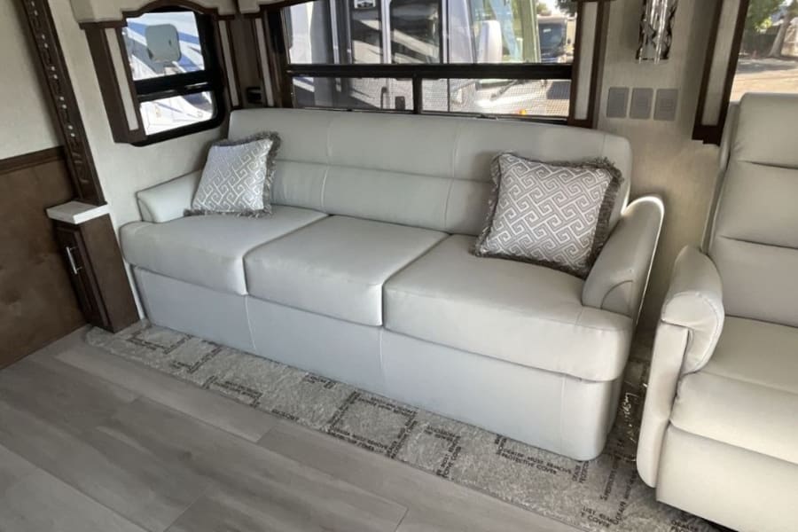 RV rental living space with a comfy white sofa, patterned pillows, and a recliner, ideal for relaxing travel.