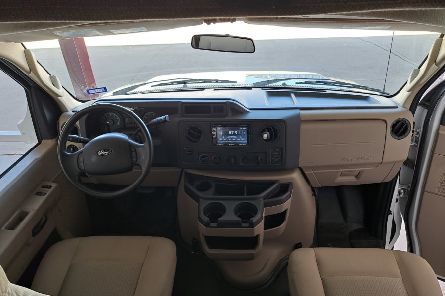 RV rental: The spacious Ford E-Series cockpit, dashboard, steering wheel, and front seats, viewed from the rear.