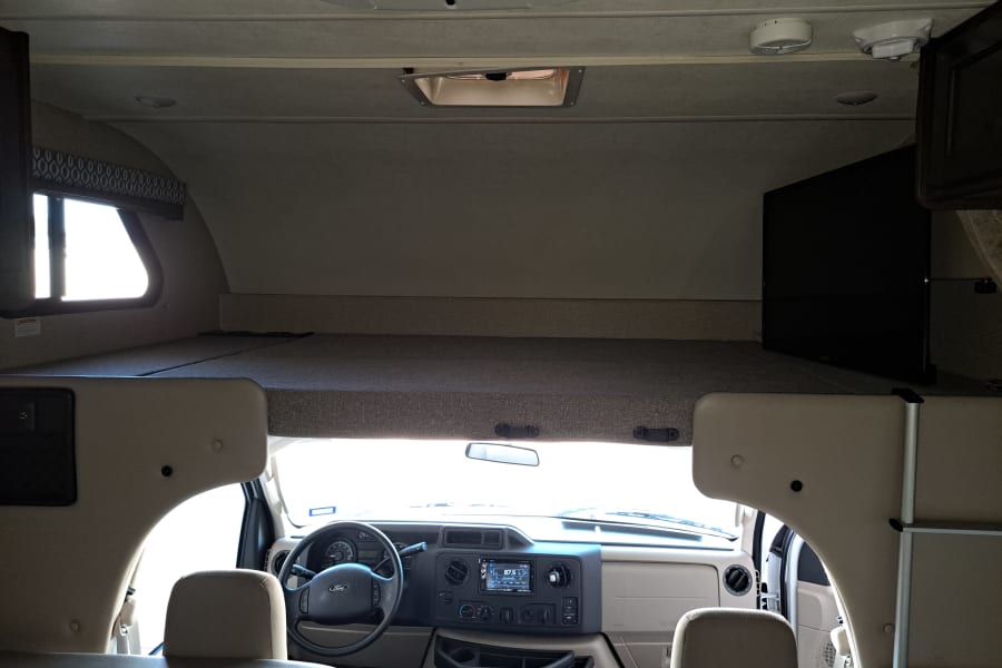 Inside an RV rental: spacious cab-over bunk, driver's cockpit, and a TV for entertainment.