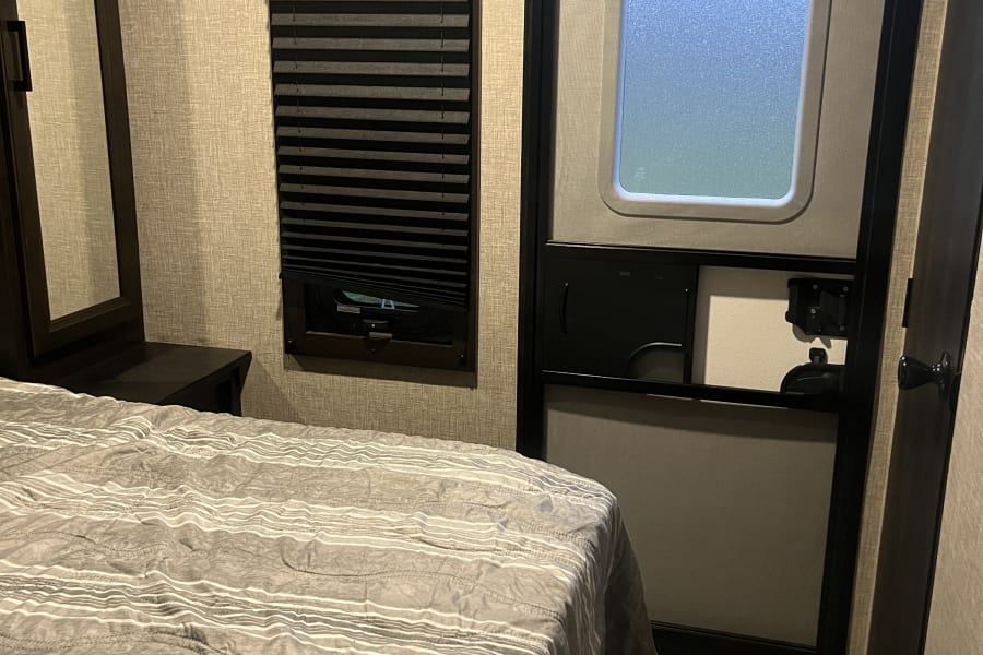 Cozy RV rental bedroom with striped comforter, window blinds, and an RV door, offering comfort.