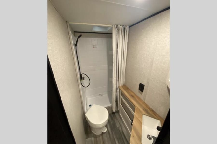 This RV rental's compact bathroom includes a shower, toilet, and a vanity with sink. A space-saving design for travel comfort.