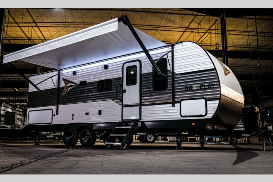 A modern white and grey travel trailer with a large extended awning, perfect for an rv rental experience.