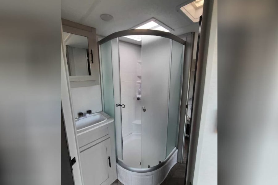 Clean RV rental bathroom with a curved glass shower, small vanity, and mirror, designed for comfortable travel.