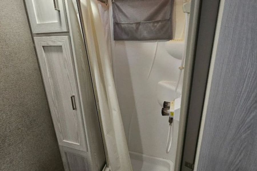 Clean, functional RV rental bathroom featuring a space-saving corner shower, toilet, and built-in storage cabinets.