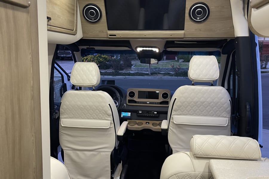 Premium RV rental interior with cream quilted seats, wood accents, TV, and a spacious front cabin view.