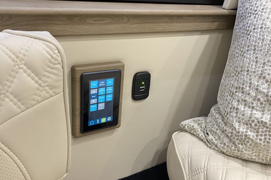 Comfortable RV rental interior: cream quilted seats, a digital touchscreen for light control, USB charging port, and cup holder.