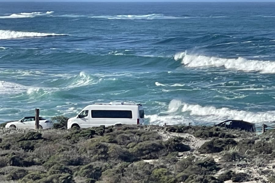 Scenic coastal view: an RV rental and other vehicles parked on a bluff overlooking the ocean with breaking waves.