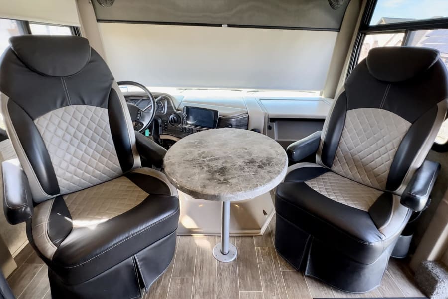 Front of an RV rental with two patterned captain's chairs, a central round table, and the dashboard area.