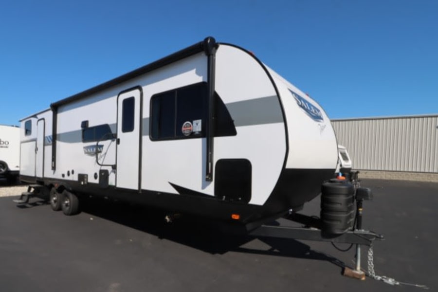 A sleek white travel trailer RV with black accents, ready for rv rental adventures. Parked on asphalt under blue sky.