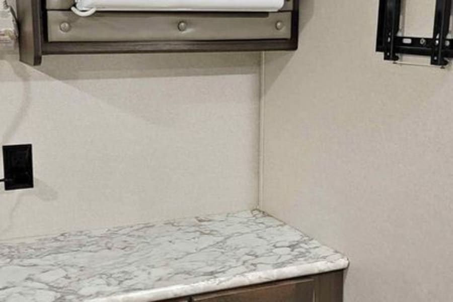 RV rental interior showcasing a mounted AC unit, marble-patterned counter, dark cabinets, and TV bracket.