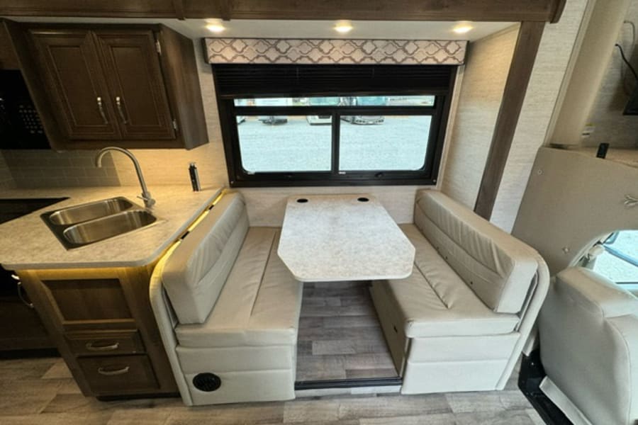 Inside an RV rental: a compact kitchen with double sink and a cozy dinette with two light-colored benches and a table.