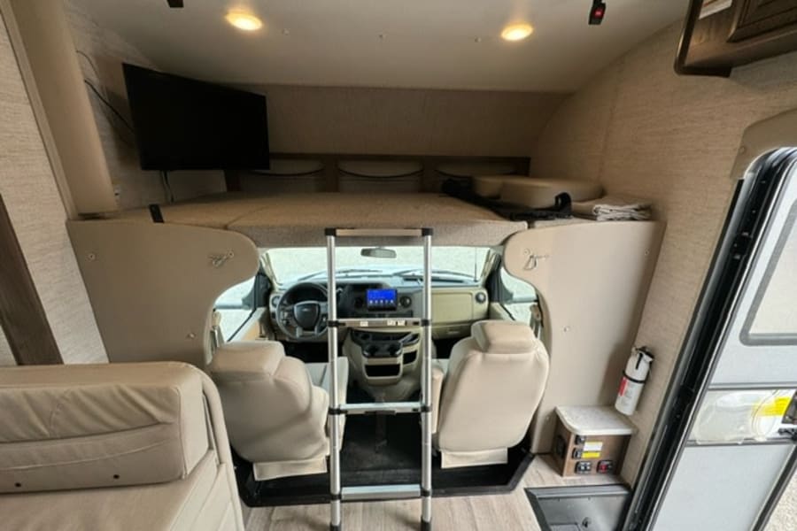 RV rental interior: front view with cab-over bunk, TV, swivel seats, and driver's area.