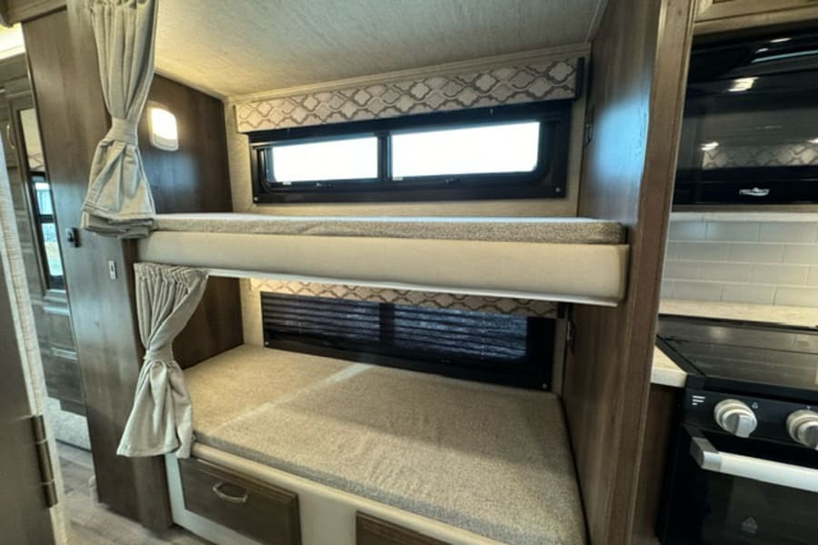 This RV rental offers a well-designed interior with comfortable bunk beds, privacy curtains, and a compact kitchen.