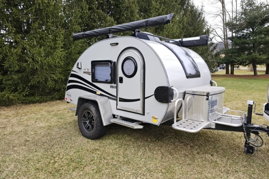 This compact teardrop travel trailer, ideal for rv rental, features a unique round door, roof awning, and front storage box.
