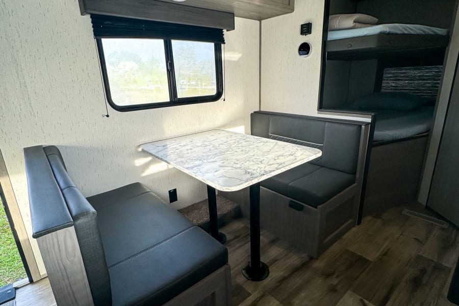 Inside an RV rental: light-filled dinette with marble-look table, storage cabinets, and twin bunk beds.