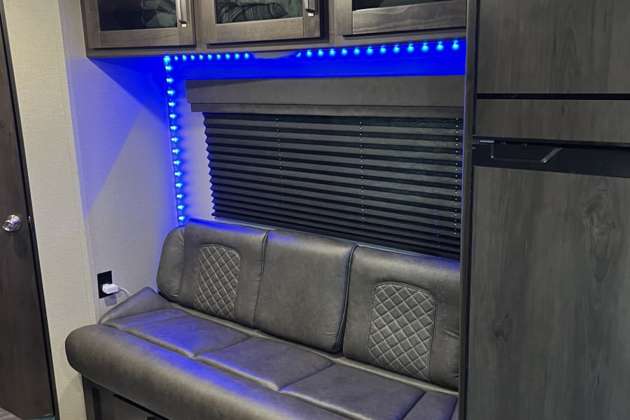 Cozy RV rental interior showing a sofa with storage, overhead cabinets, blue LED lighting, and a refrigerator.