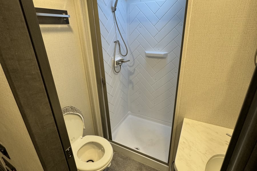 Compact RV rental bathroom featuring a white toilet, glass-enclosed shower, and small vanity with sink.