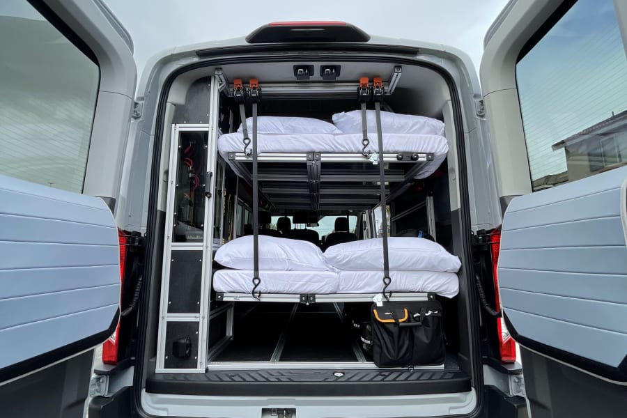 Rear view of a grey van converted for RV rental, featuring a custom interior with two stacked bunks & storage solutions.