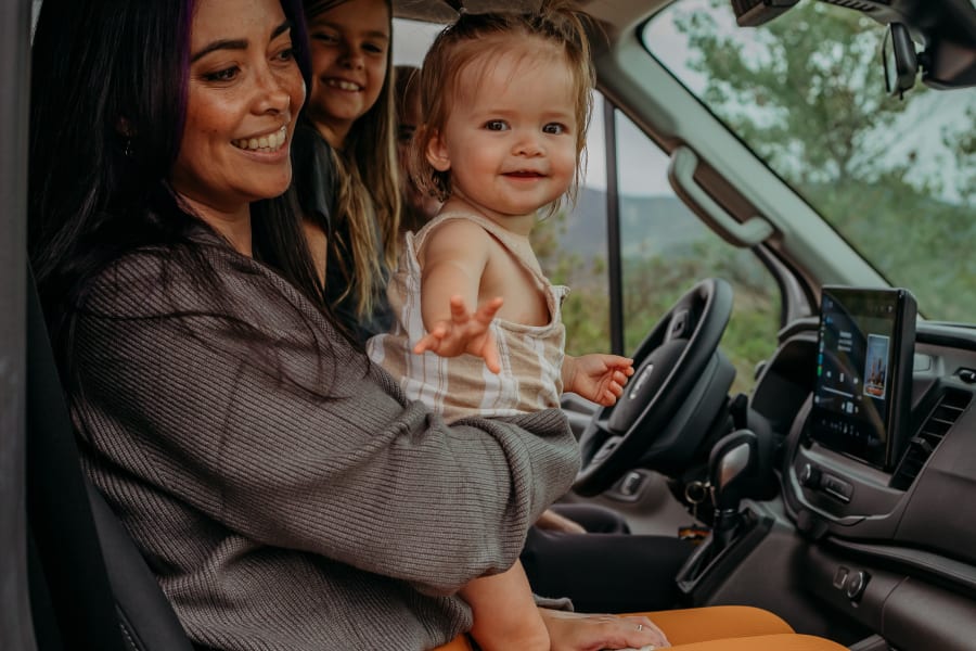 Smiling mom holds a baby with another child in their cozy rv rental, ready for family adventures.