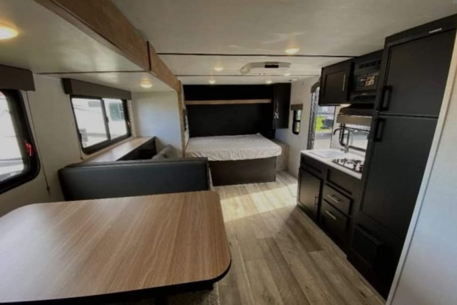 Modern RV rental interior with dining table, booth seating, bed, and fully equipped kitchen area.