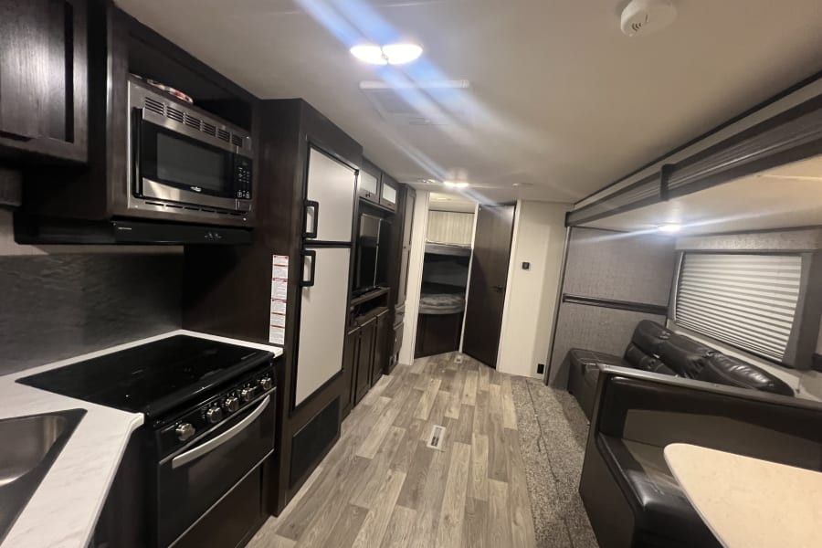 Inside this modern RV rental: a well-equipped kitchen, comfortable dining booth, and a peek into the bunk bed area. Enjoy your road trip!