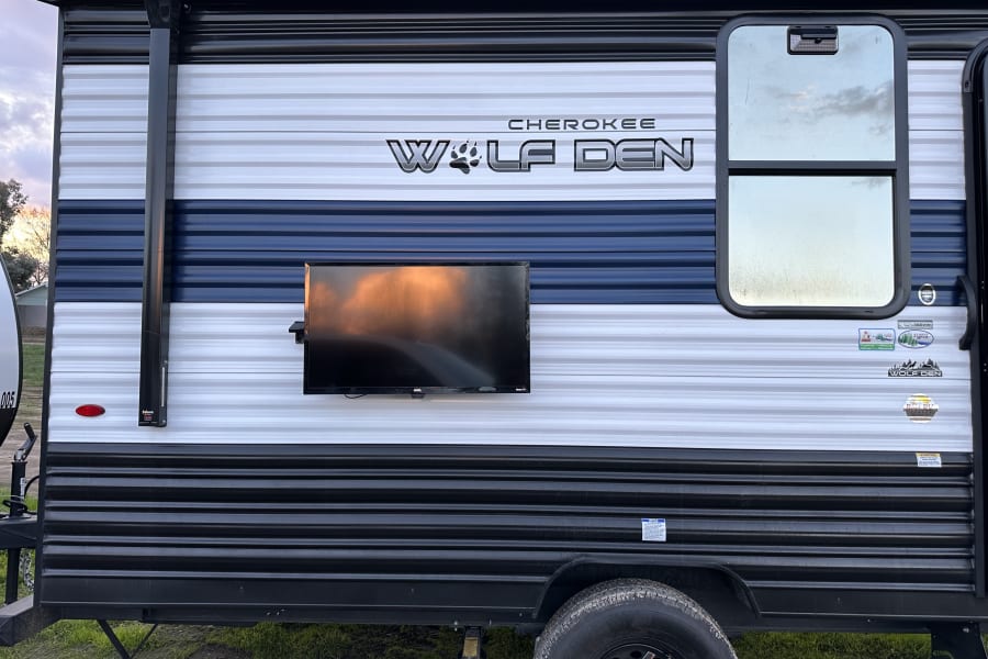 Cherokee Wolf Den RV rental side view with outdoor TV, awning, and distinctive white, blue, and black stripe pattern.