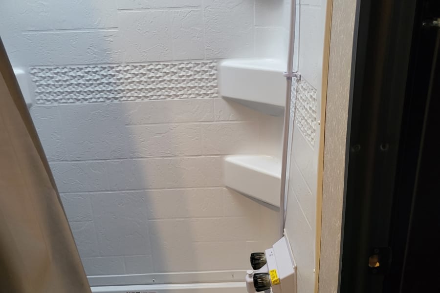 RV rental bathroom: A clean, white shower with textured wall tiles, a decorative band, and built-in corner shelves.