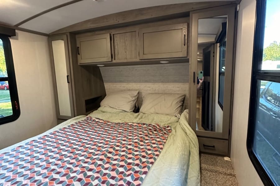 This RV rental bedroom features a comfy bed with a colorful geometric blanket, overhead storage, and a full-length mirrored closet.
