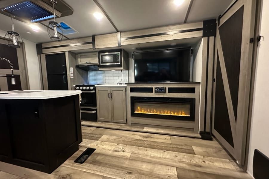 Experience an RV rental: modern kitchen with island, a living area boasting a TV & electric fireplace. Cozy travel awaits!