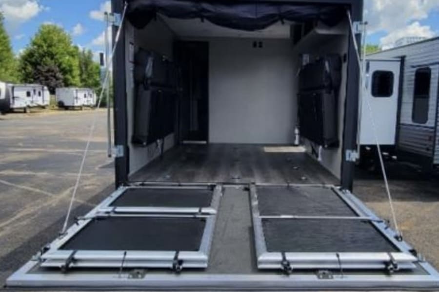 Spacious toy hauler RV rental: ramp door lowered, revealing versatile cargo area with fold-up beds. Perfect for your adventures.