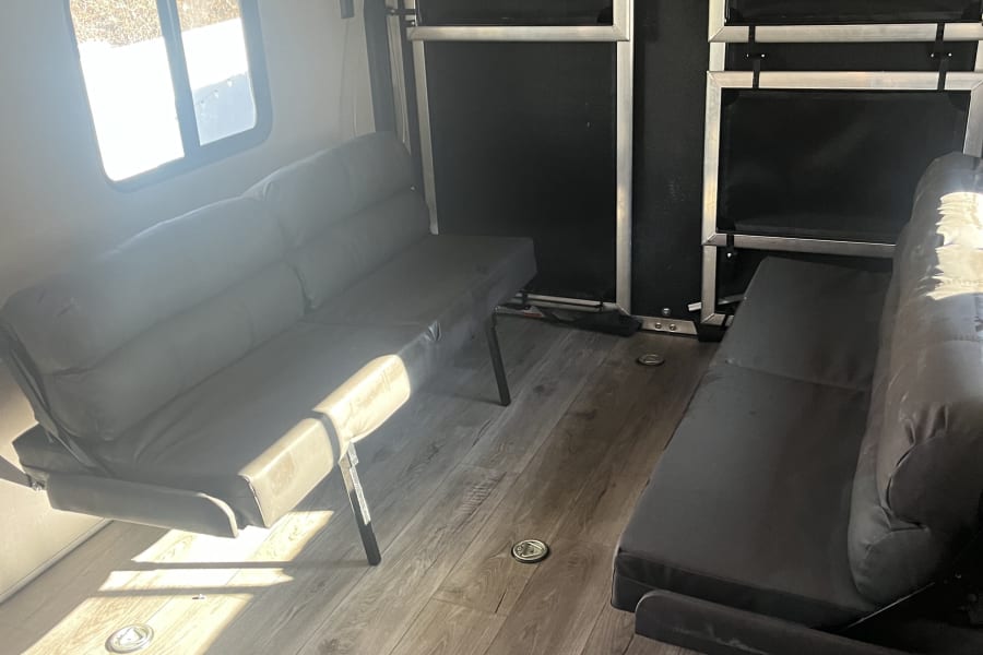 RV rental toy hauler interior featuring dual fold-down sofas/beds, wood-look floor, and cargo tie-downs.