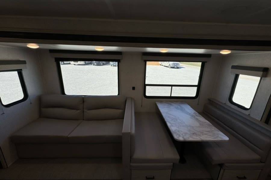 Spacious RV rental interior featuring a comfy sofa, dinette with marble-patterned table, and multiple windows.