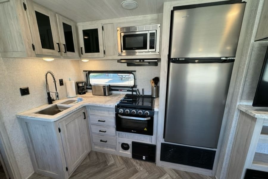 Spacious rv rental kitchen with light wood cabinetry, stainless steel fridge, microwave, and stove.