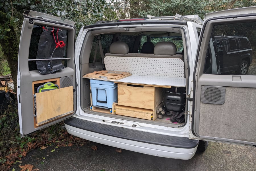 Inside an open RV rental van, a custom camper conversion features integrated kitchen, cooler, and storage solutions.