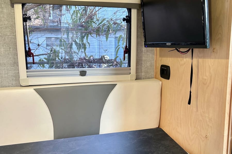 An RV rental's dinette area, featuring a window, wall-mounted TV, table, and control panel on the wood interior.